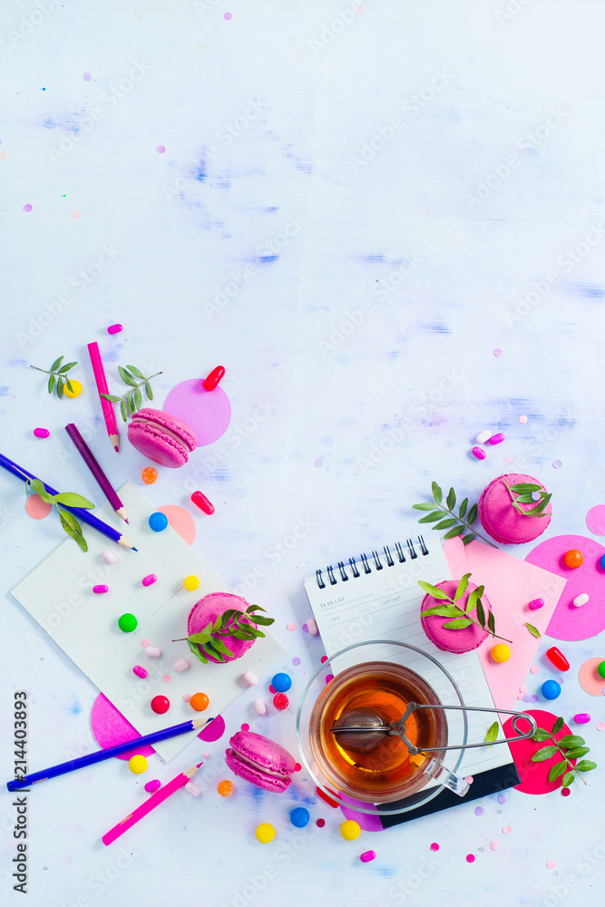 Planning a party concept. Notepad with to-do list, sweets, confetti and macaroon cookies with tea. Colorful objects in high key with copy space.