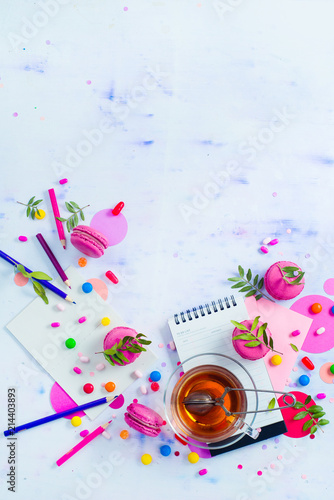 Planning a party concept. Notepad with to-do list, sweets, confetti and macaroon cookies with tea. Colorful objects in high key with copy space.