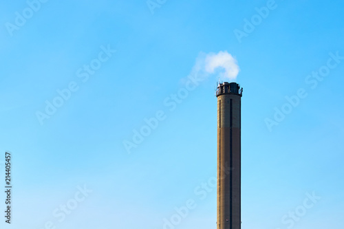 Industrial pipe with smoke against a blue sky. Copy space for text. 