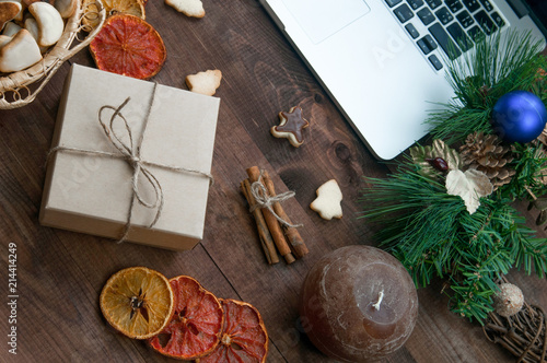 Christmas working place, Christmas gift boxes, dry oranges, cinnamon and ginger cookies on brown wooden table with computer.