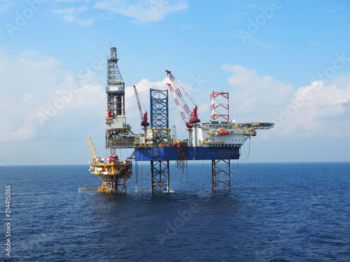 Jack up rig is set up for drilling operations over offshore static platform with blue sea and skies background.