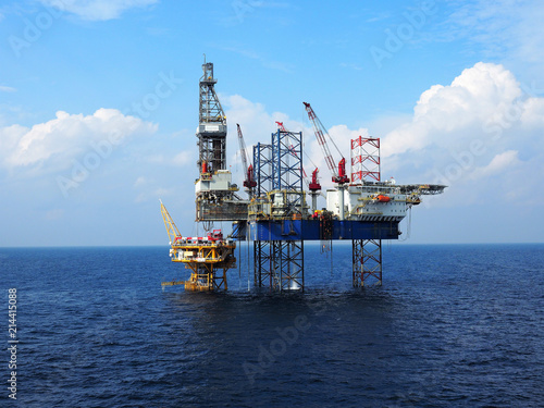 Jack up rig is set up for drilling operations over offshore static platform with blue sea and skies background.