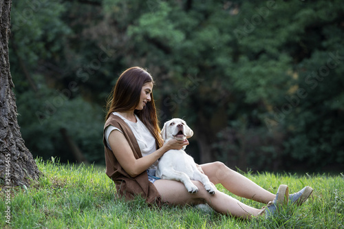 young womand sitting on the ground in park and holding her dog photo