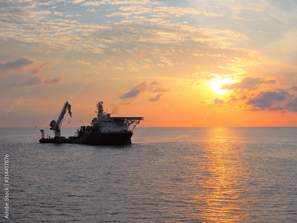 Construction support vessel positions next to static platform with sun rise background.