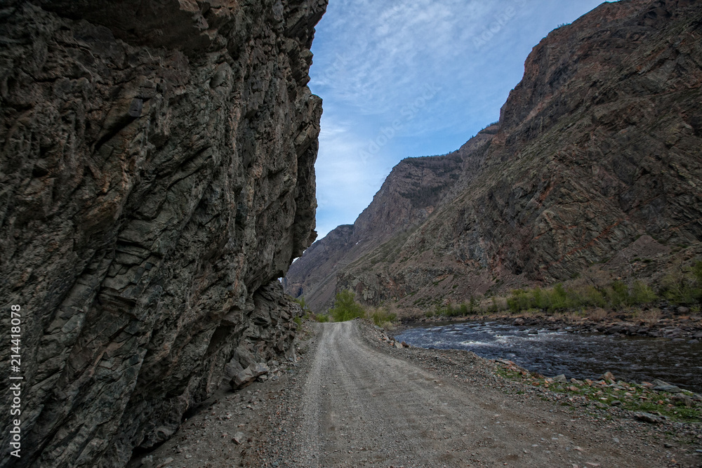 dirt road along a mountain river between vertical walls of rocks