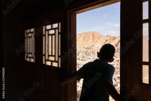 Naughty boy looking through the wooden ancient door to old town of Leh city from Leh palace in Leh Ladakh, Jammu and Kashmir, India