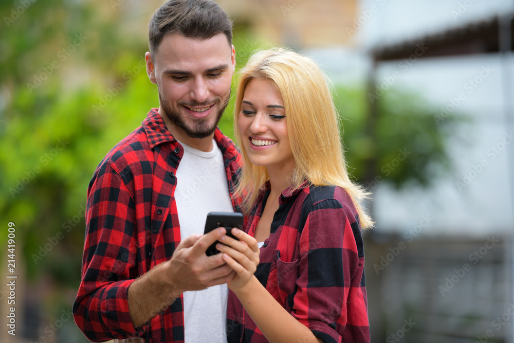 Young couple using phone together in the streets outdoors Young couple using phone together in the streets outdoors