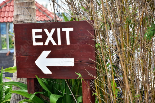 EXIT. The inscription on a wooden dark board. The arrow indicates the direction. Pointer on a background of palms and bamboo
