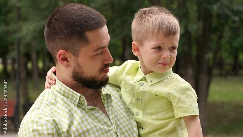 A young father holds a little crying boy in his arms, the mother comes to them and kisses the upset child. A young father holds a little crying boy in his arms, the mother comes to them and kisses the upset child.