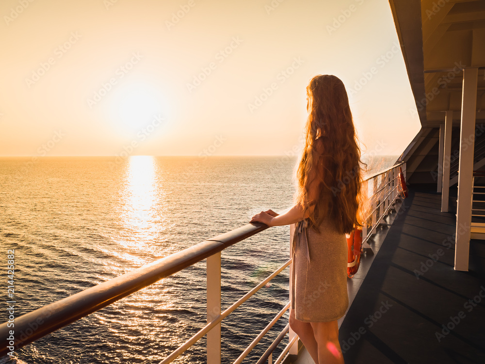 Stylish, beautiful woman on an empty deck of a cruise ship against a background of sea waves, blue sky and sunset - obrazy, fototapety, plakaty 
