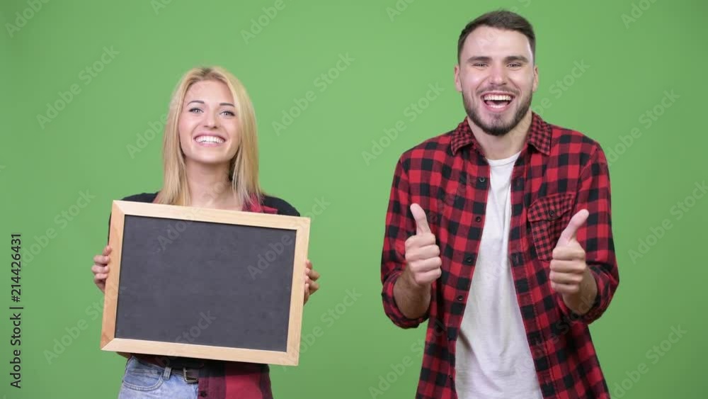 Young couple holding blackboard giving thumbs up together Young couple holding blackboard giving thumbs up together