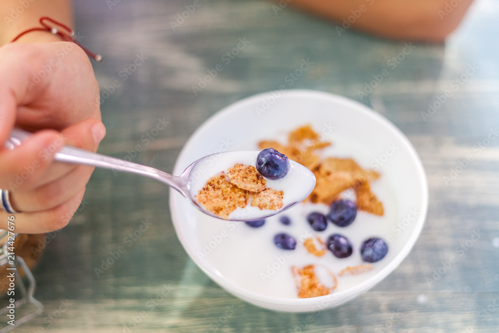 A woman is eating yogurt with cereal and berries for breakfast, holding a spoon, close-up hands, a healthy diet and a diet concept, summer berries A woman is eating yogurt with cereal and berries for breakfast, holding a spoon, close-up hands, a healthy diet and a diet concept, summer berries