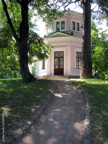 A steep path with two mighty trees on either side leading to a building with pink walls