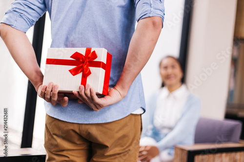 Obraz na plátne Middle aged husband hiding a surprise gift and roses for surprising his wife on special day such as birthday or wedding anniversary