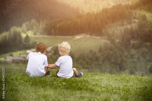 Two boys sit on the hill and talking cheerfully. Back view