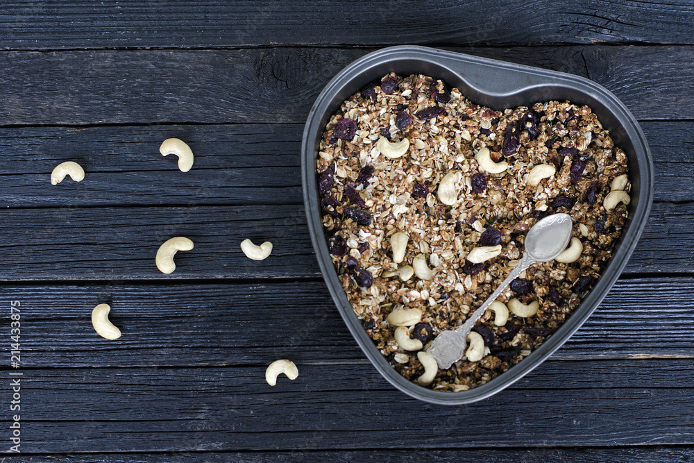 Granola with cashews in a baking sheet. Black wooden table Granola with cashews in a baking sheet. Black wooden table