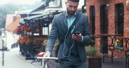 TRACKING Handsome young adult man wearing suit choosing music on his phonee before riding his classic bicycle to work in the morning. 4K UHD 60 FPS SLOW MOTION photo