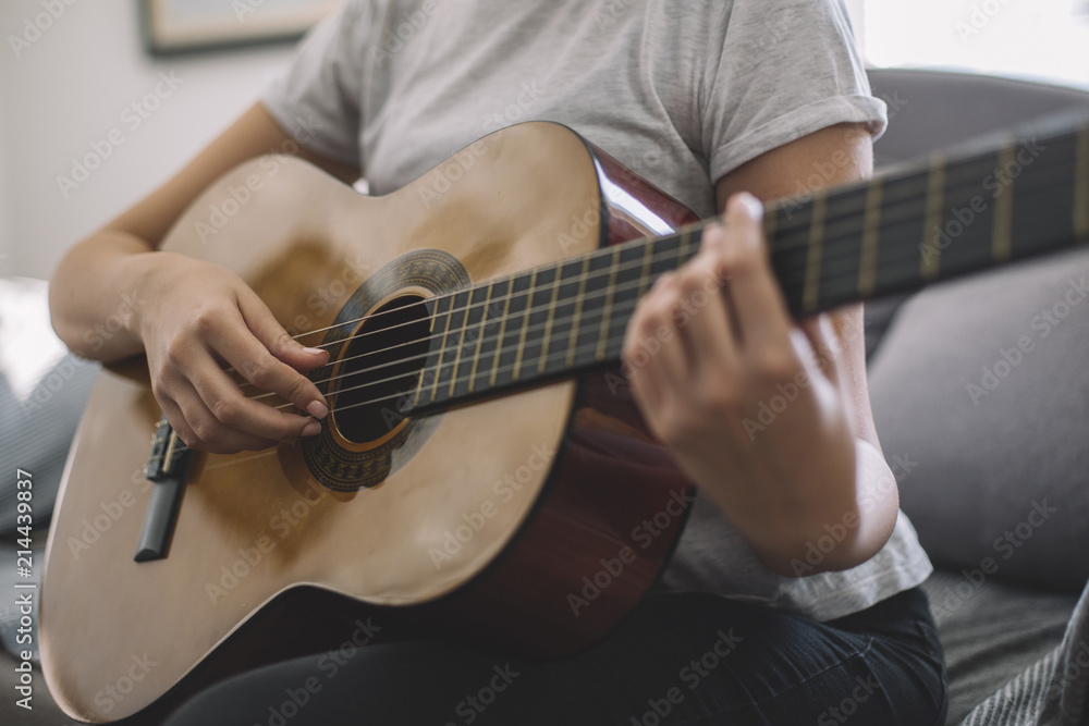 Fototapeta premium A young girl learns to play guitar. Woman's hands playing acoustic guitar.