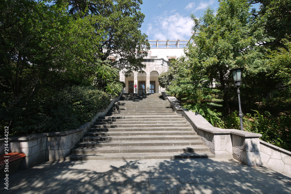 Wide stone steps with three arches at the entrance of the building against the backdrop of green trees and a blue sky