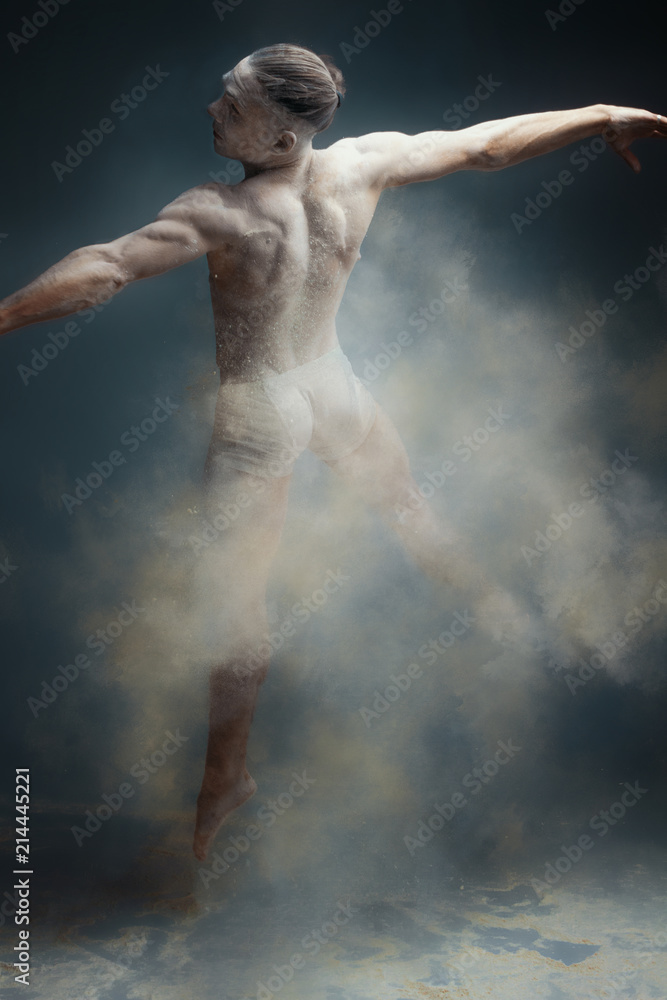 Dancing in flour concept. Muscle fitness guy man male dancer in dust / fog. Guy wearing white shorts making dance element in flour cloud on isolated grey background Dancing in flour concept. Muscle fitness guy man male dancer in dust / fog. Guy wearing white shorts making dance element in flour cloud on isolated grey background