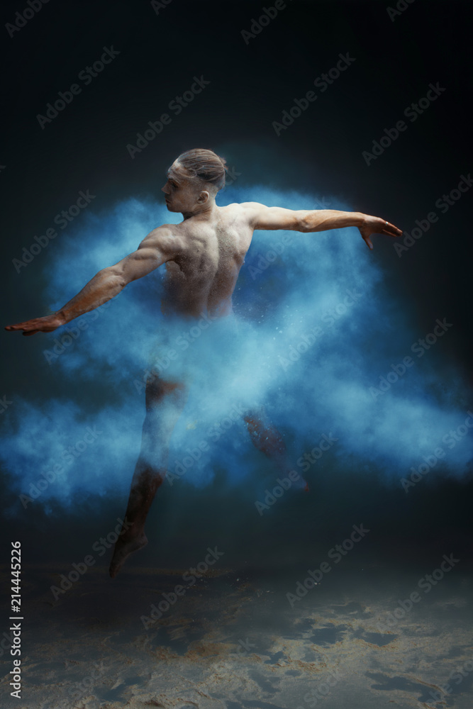 Dancing in flour concept. Muscle fitness guy man male dancer in light blue dust / fog. Guy making dance element in flour cloud. Blue ribbon as a symbol of bowel cancer concept.