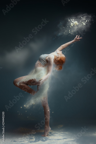 Dancing in flour concept. Redhead beauty female girl adult woman dancer in dust / fog. Girl wearing white top and shorts making dance element in flour cloud on isolated grey / black background
