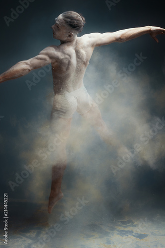 Dancing in flour concept. Muscle fitness guy man male dancer in dust / fog. Guy wearing white shorts making dance element in flour cloud on isolated grey background