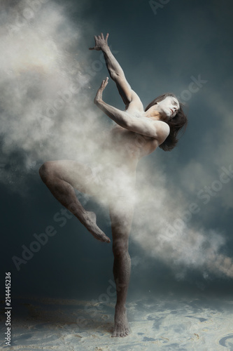 Dancing in flour concept. Long hair muscle fitness guy man male dancer in dust / fog. Guy wearing white shorts making dance element in flour cloud on isolated grey / black background