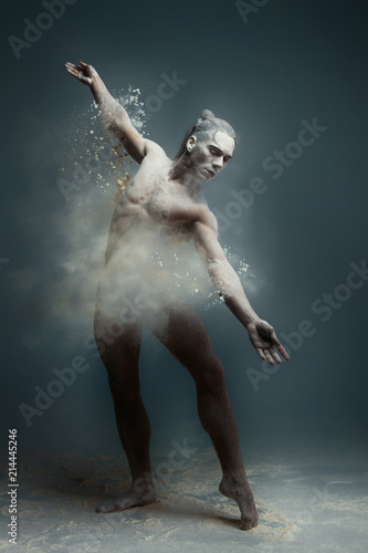 Dancing in flour concept. Long hair muscle fitness guy man male dancer in dust / fog. Guy wearing white shorts making dance element in flour cloud on isolated grey / black background
