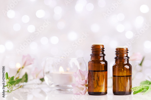 Two bottles with essential oil, flowers and candles on white table with bokeh effect. Spa, aromatherapy, wellness, beauty background.