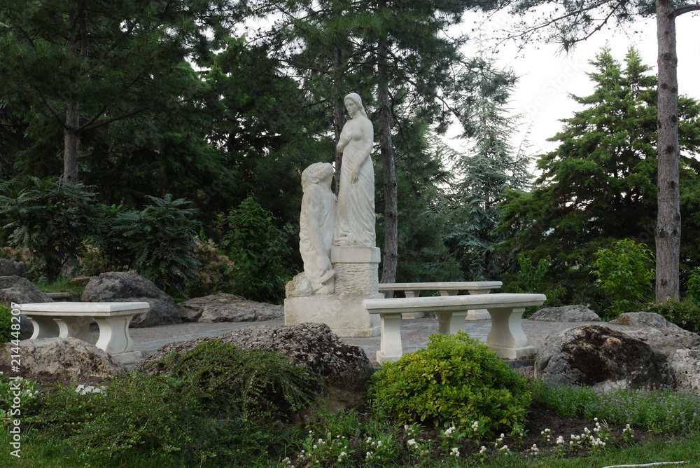 white statue of a frail woman with her husband sculptor on the background of majestic pisoners in the park