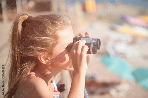 cute little caucasian girl holding binoculars watching far away on beach