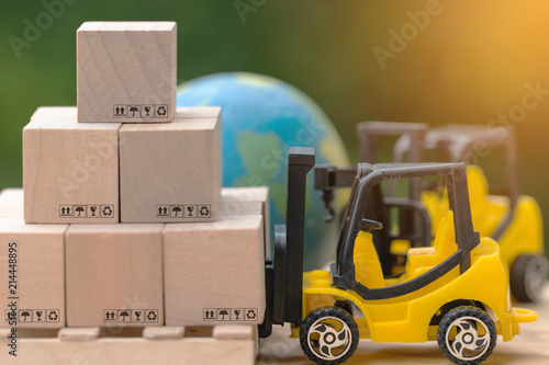 Mini forklift trucks load stack of cardboard boxes on wooden pallet with nature background and globe. Logistics and transportation management ideas and Industry business commercial concept.