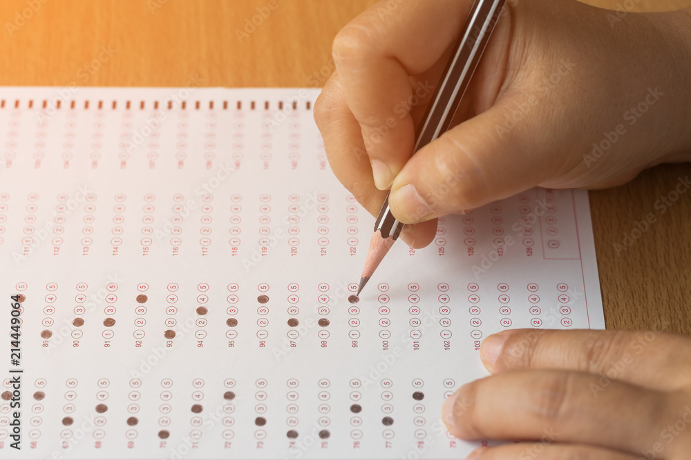 Student's hands filling in standardized test form with black pencil drawing selected choice on answer sheets. Ideas about education. Student's hands filling in standardized test form with black pencil drawing selected choice on answer sheets. Ideas about education.