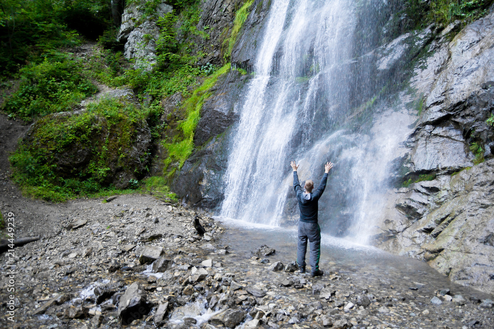 Obraz premium man standing by waterfalls with arms outstretched in the air