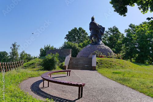 High statue of a knight under a blue sky on the background of beautiful green trees