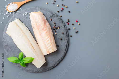 Fresh raw cod fillet with spices, pepper, salt, basil on stone plate, horizontal, copy space, top view