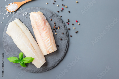 Fresh raw cod fillet with spices, pepper, salt, basil on stone plate, horizontal, copy space, top view photo
