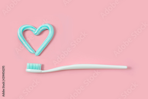 Toothbrushes and turquoise color toothpaste in shape of heart on pink background. Dental and healthcare concept.