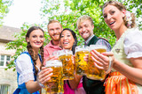 Five friends, men and women, having fun in beer garden clinking glasses with beer