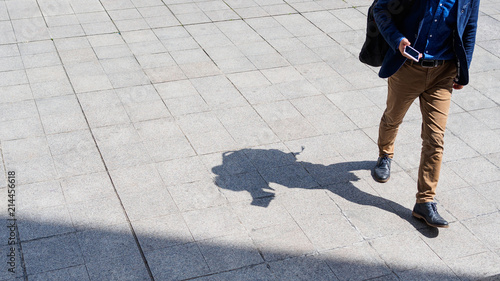 Business man walking and texting on his mobile phone on pedestrian with black silhouette shadow on ground. 