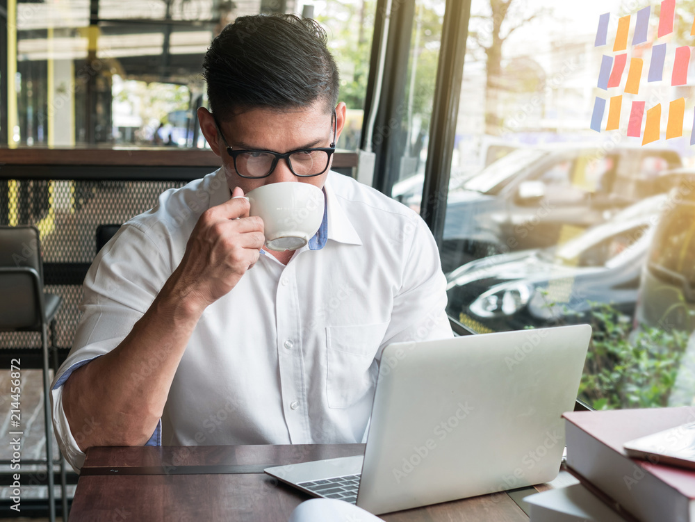 Businessman drinking coffee or tea while using laptop computer in a coffee shop Businessman drinking coffee or tea while using laptop computer in a coffee shop