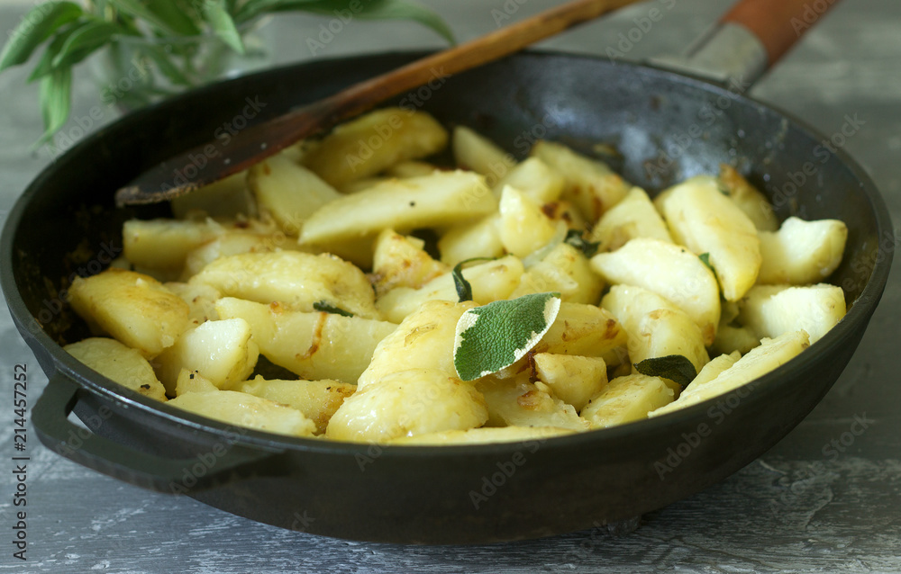 Young fried potatoes with onions and sage in a frying pan on a concrete table. Young fried potatoes with onions and sage in a frying pan on a concrete table.