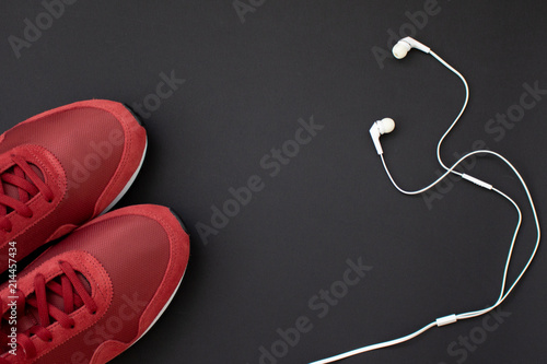 Fitness flat lay. Healthy lifestyle and sport concept. Red sneakers and white earphones on a black background.