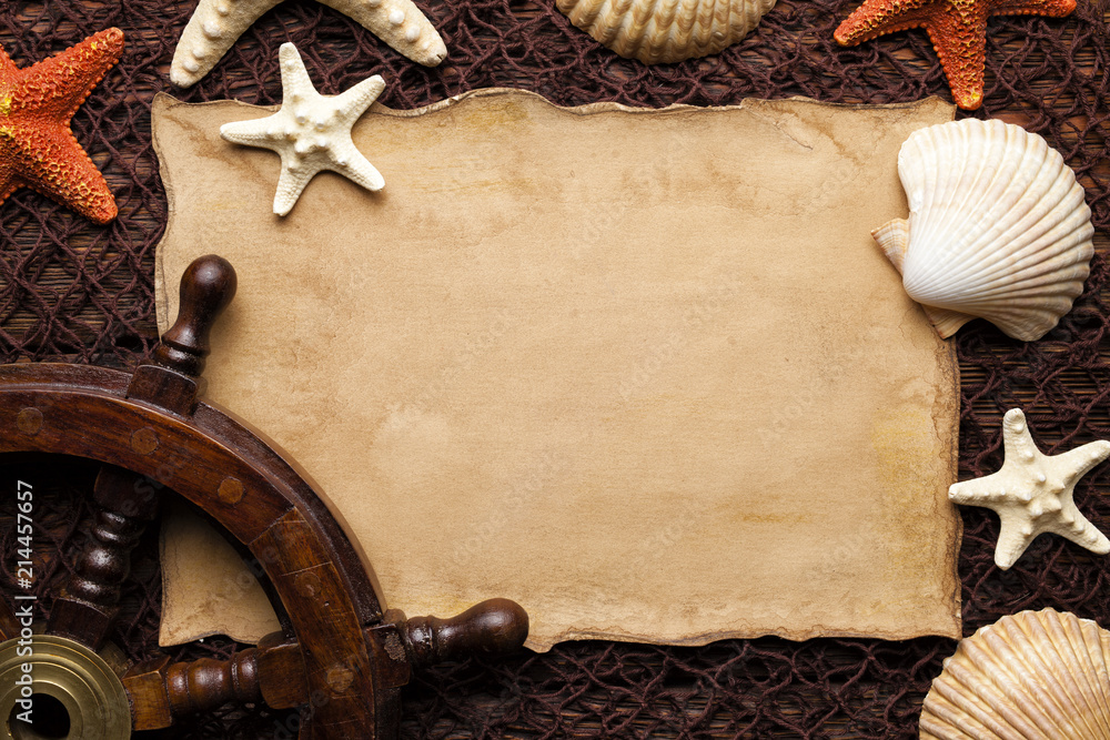 Blank paper sheet, shells and ship's steering wheel on brown fishing net Blank paper sheet, shells and ship's steering wheel on brown fishing net