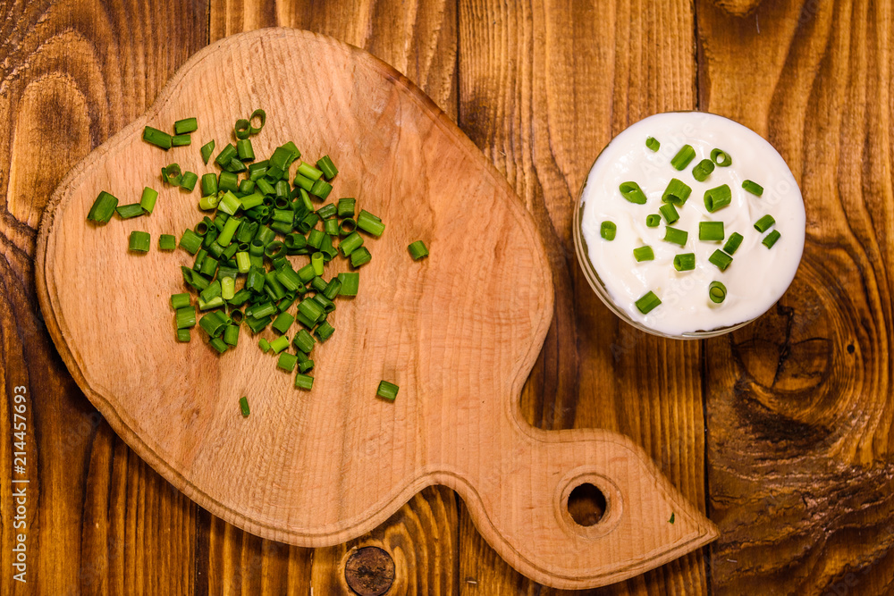 Glass bowl with sour cream and cutting board with chopped green onion on wooden table. Top view Glass bowl with sour cream and cutting board with chopped green onion on wooden table. Top view