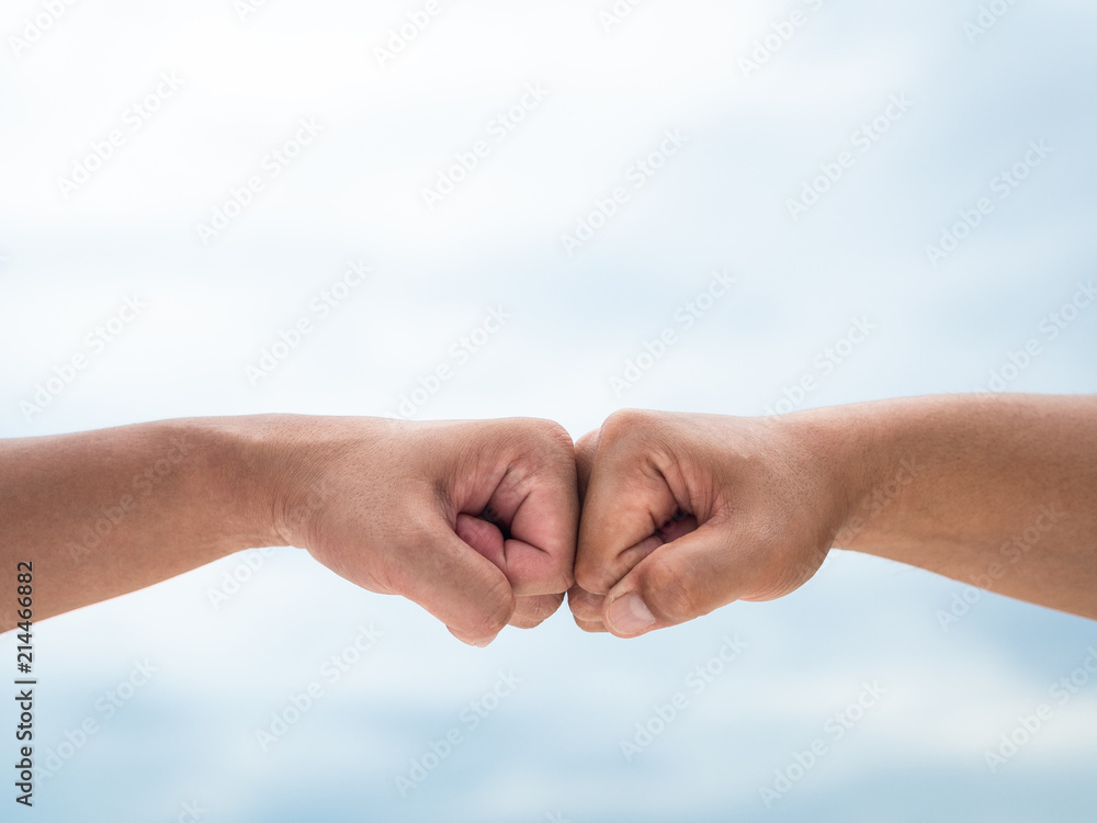 Closeup young man fist bump on the blue sky sea background. Friendship & Teamwork Concept.