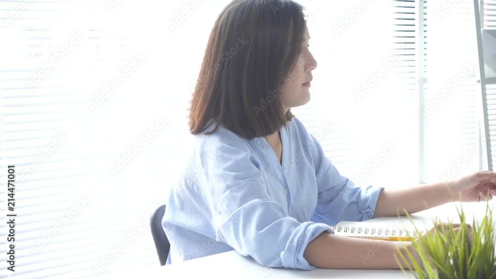 Slow motion - Beautiful young smiling woman working on laptop while enjoying drinking warm coffee sitting in a living room at home. Enjoying time at home. Asian business woman working in home office. Slow motion - Beautiful young smiling woman working on laptop while enjoying drinking warm coffee sitting in a living room at home. Enjoying time at home. Asian business woman working in home office.