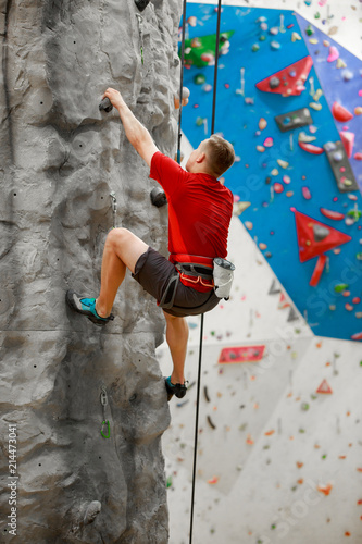 Photo from back of sports man in red T-shirt training on climbing wall