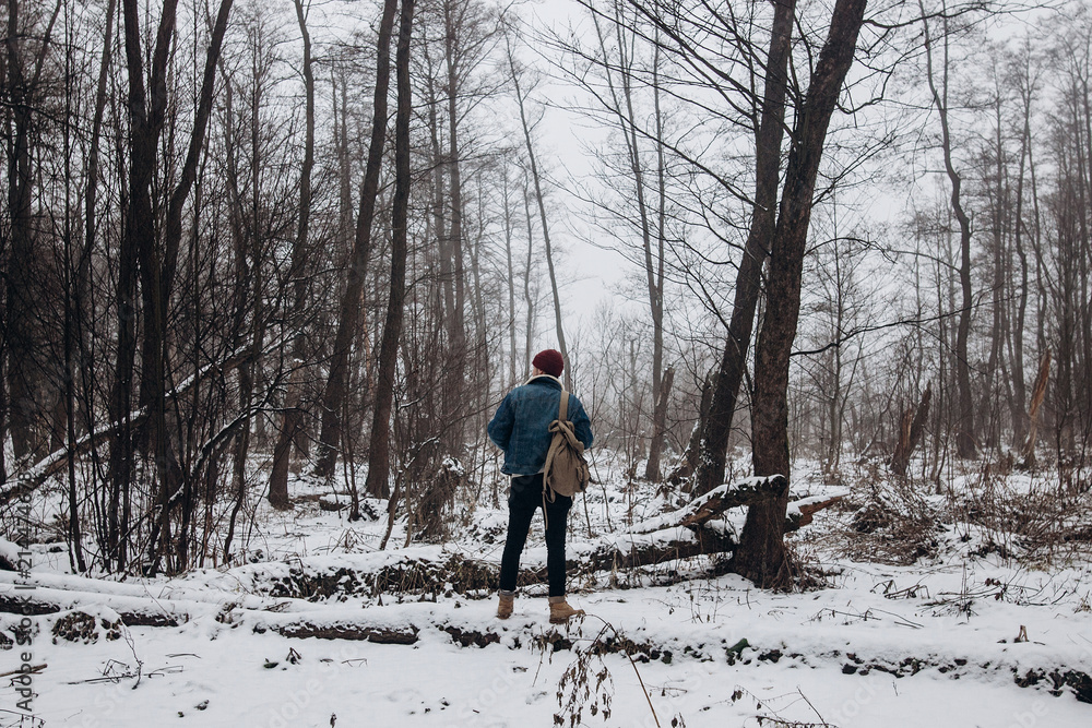 stylish hipster traveler with backpack enjoying silence in winter snowy forest trees. wanderlust and adventure concept with space for text. atmospheric moment